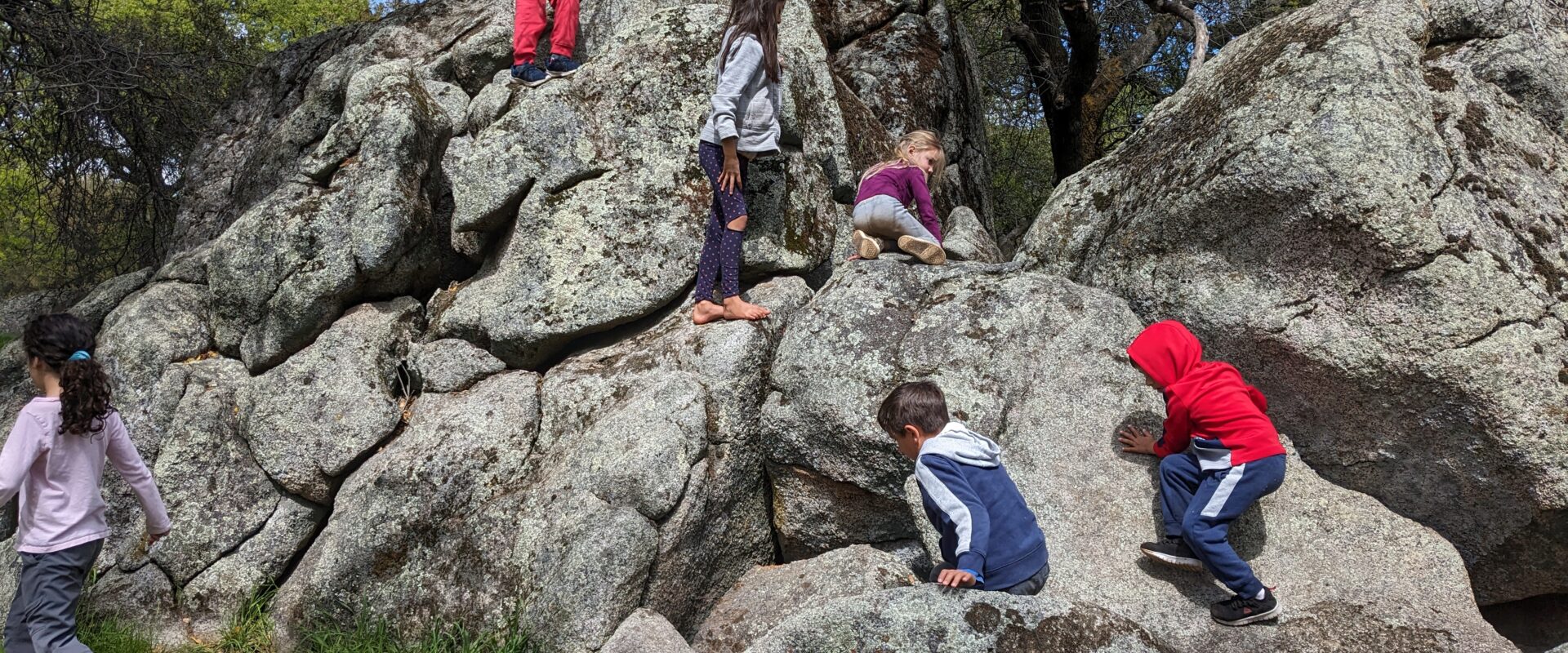 Kids climbing granite boulders in oak woodland under blue sky