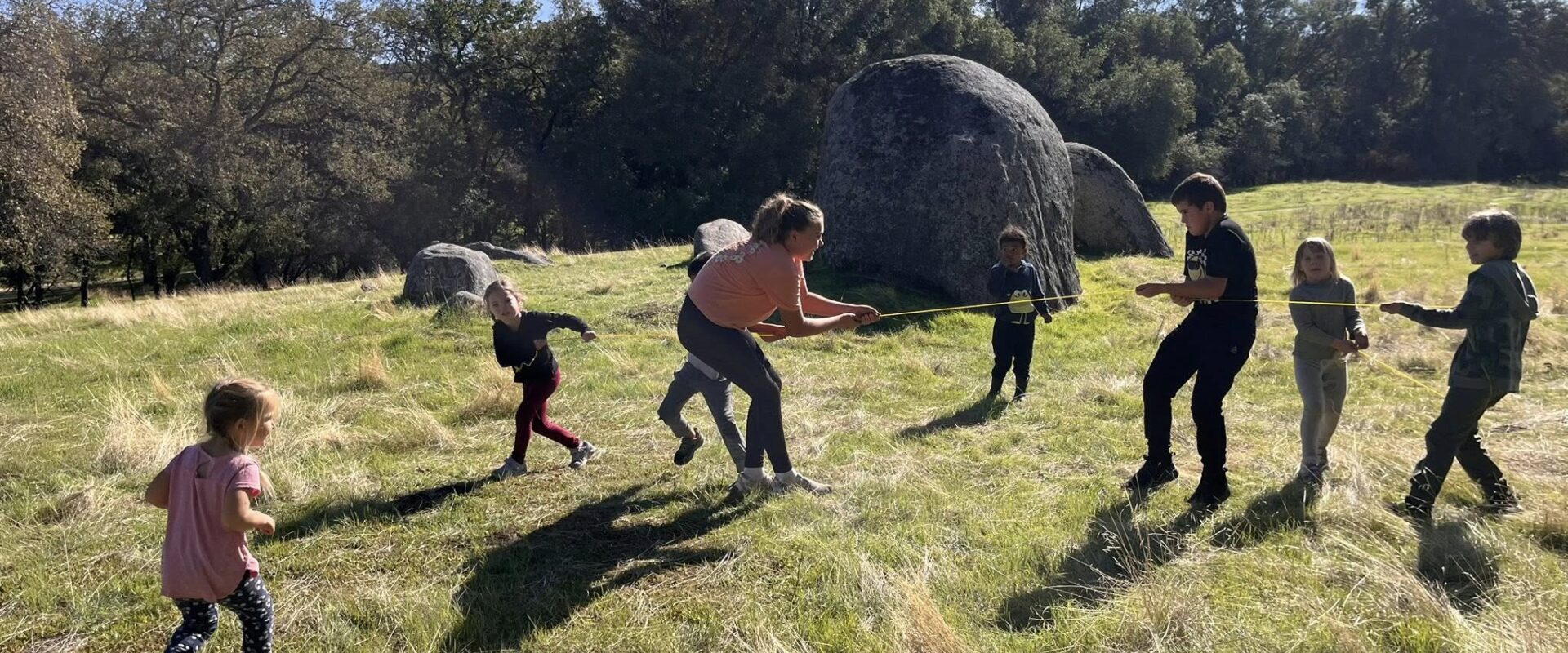 Kids and teacher playing tug-of-war in an open meadow