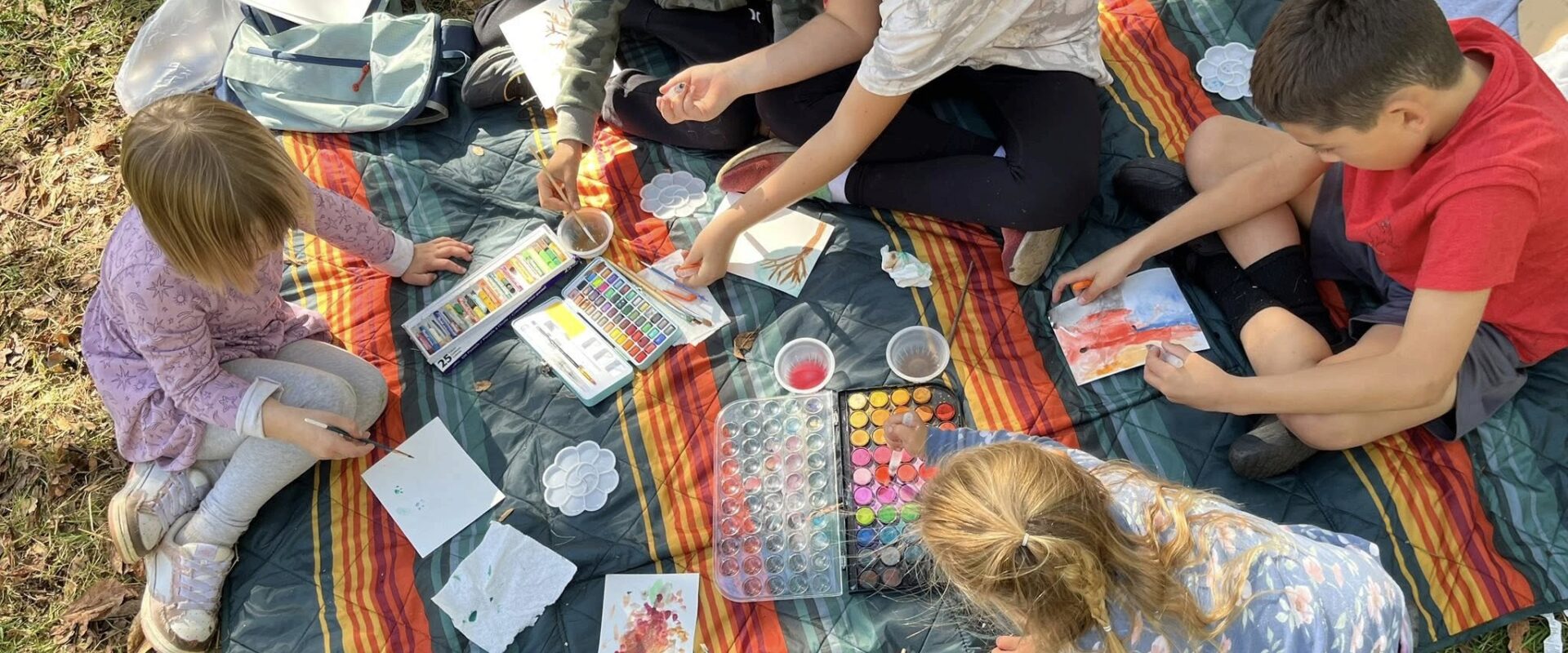 Children watercolor painting together on blankets outdoors